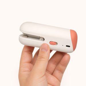 Warm white and coral rechargeable mini bag sealer held in one hand